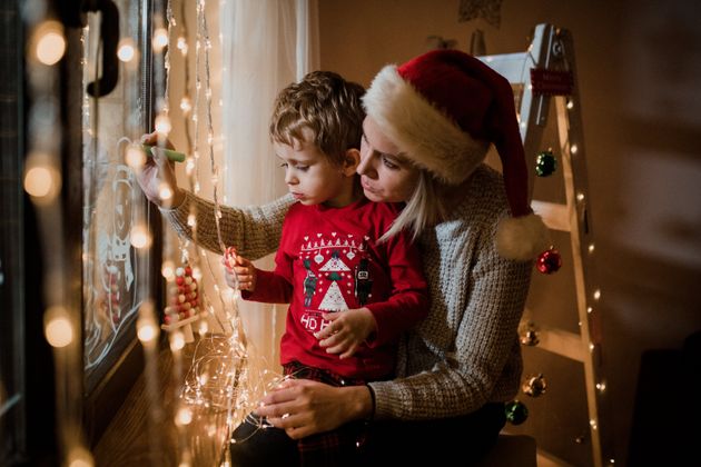 Mother and son draw Christmas holidays decoration painted on window glass.