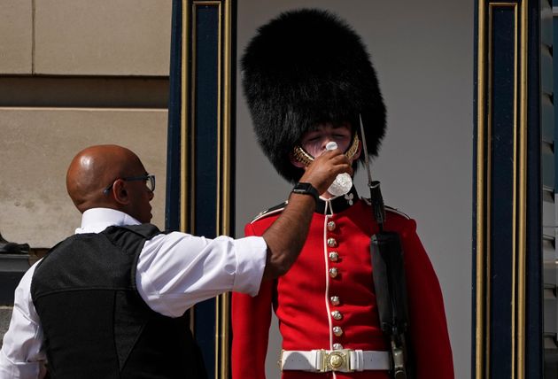 A police officer gives water to a British soldier wearing a traditional bearskin hat, on guard duty outside Buckingham Palace, during hot weather in London on Monday.