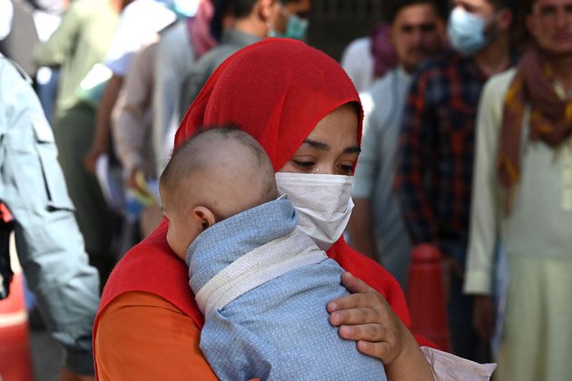 A woman with a child stands in a queue along with others to submit their passport applications at an office in Kabul days before the Taliban took complete control