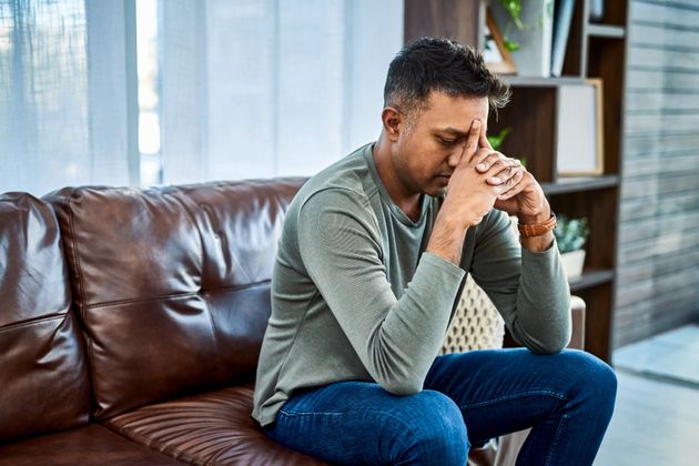 Shot of a man looking stressed while sitting on the sofa at home