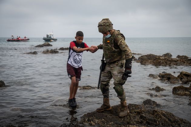 A Spanish soldier helps a migrant after he crossed the border between Morocco and Spain by swimming in May, 2021