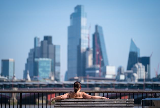 A woman soaks up the sun on the South Bank, London, looking out at the view of Blackfriars Bridge and skyscrapers in the City financial district. 