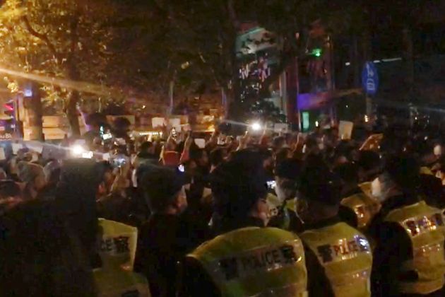 In this image from video obtained by The Associated Press, police, foreground, watch protesters in Shanghai on Saturday, Nov. 26, 2022. (AP Photo)