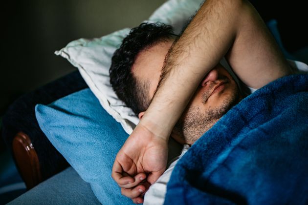 Young Caucasian man waking up in bed in late morning.