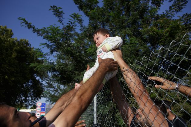 Serbia, Horgos. Group of refugees crossing holding baby over wired fence short after closing Hungarian border. 