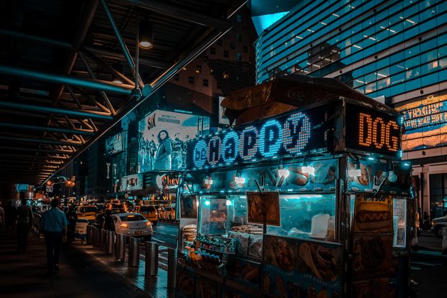 A street food stand lights up in the night in New York City, attracting passers-by to an array of late-night treats by Markus Nocker.