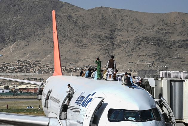 Afghan people climb atop a plane as they wait at the Kabul airport in Kabul on August 16, 2021